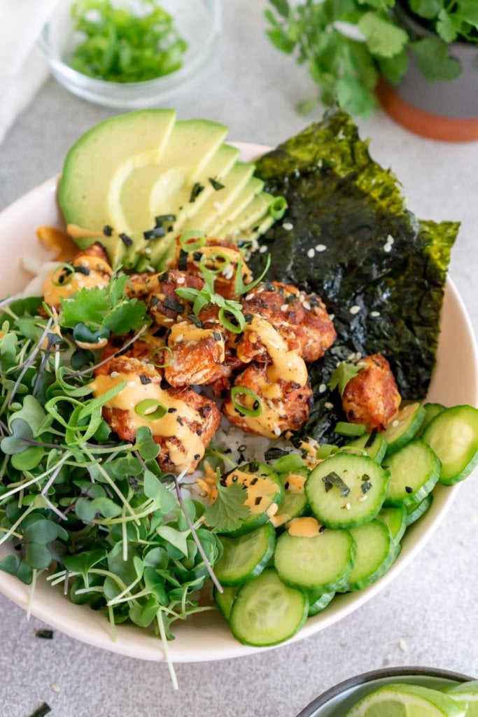 salmon rice bowl with avocado, cilantro, cucumbers, and seaweed paper