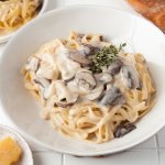 creamy mushroom pasta in a white bowl with thyme