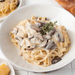 a large bowl of mushroom pasta with cream sauce and a baguette