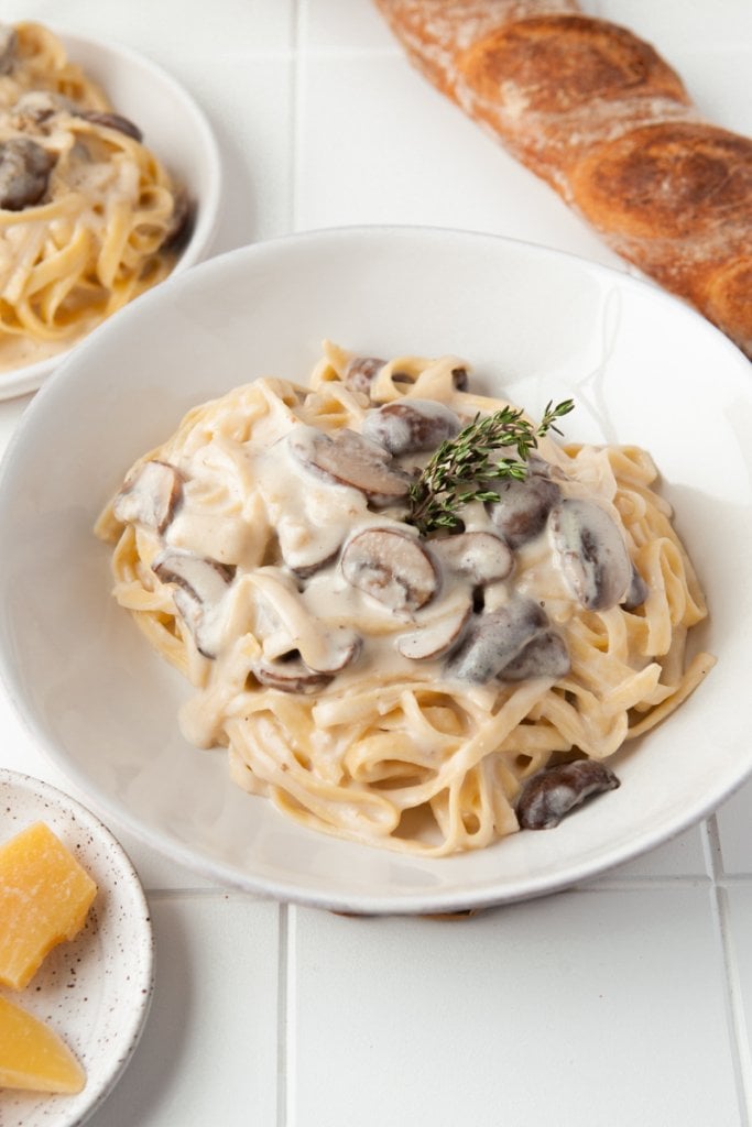 a large bowl of mushroom pasta with cream sauce and a baguette