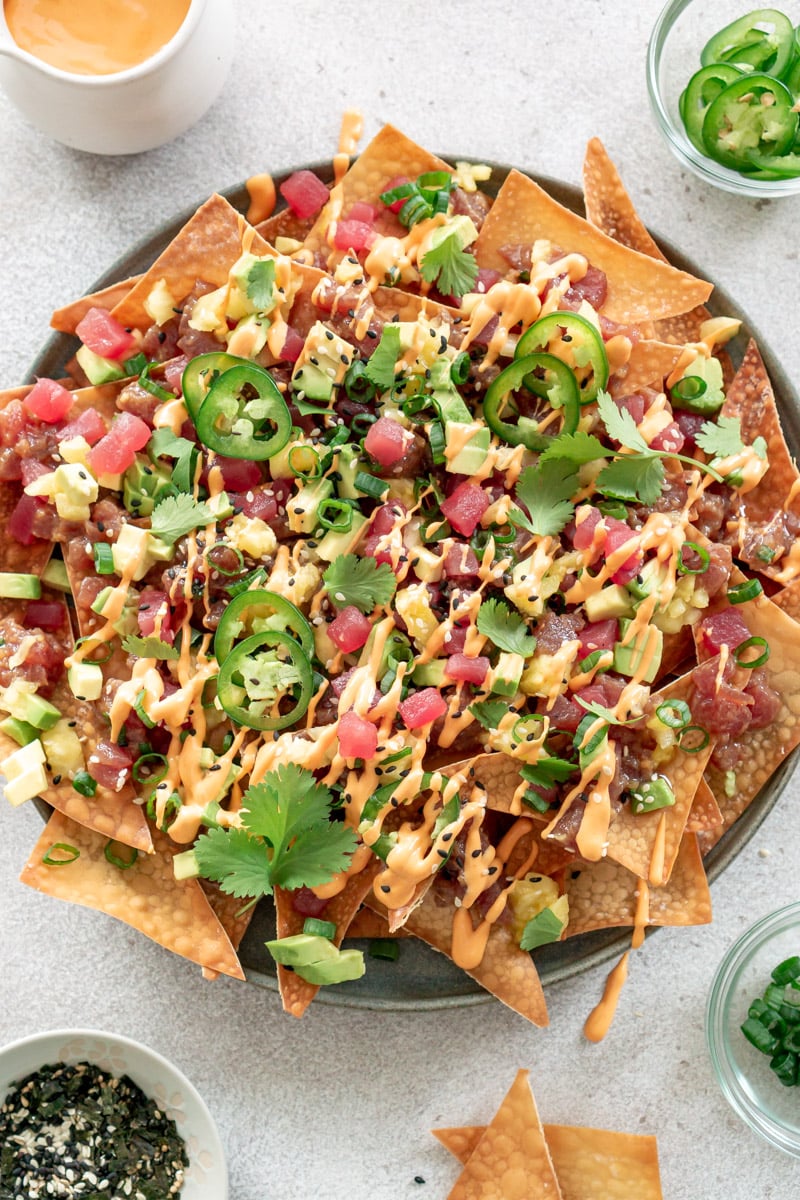 Poke nachos on a large serving plate with jalapeño and other toppings to the side.