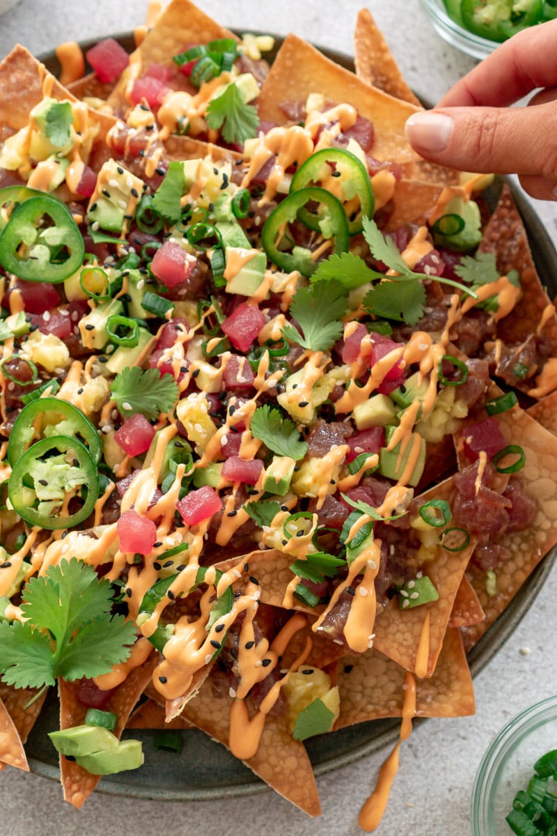 Hand grabbing a tuna poke nacho from a platter.