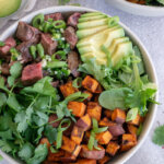 steak bowl with avocado, cilantro, and sweet potatoes with lime wedges on the side