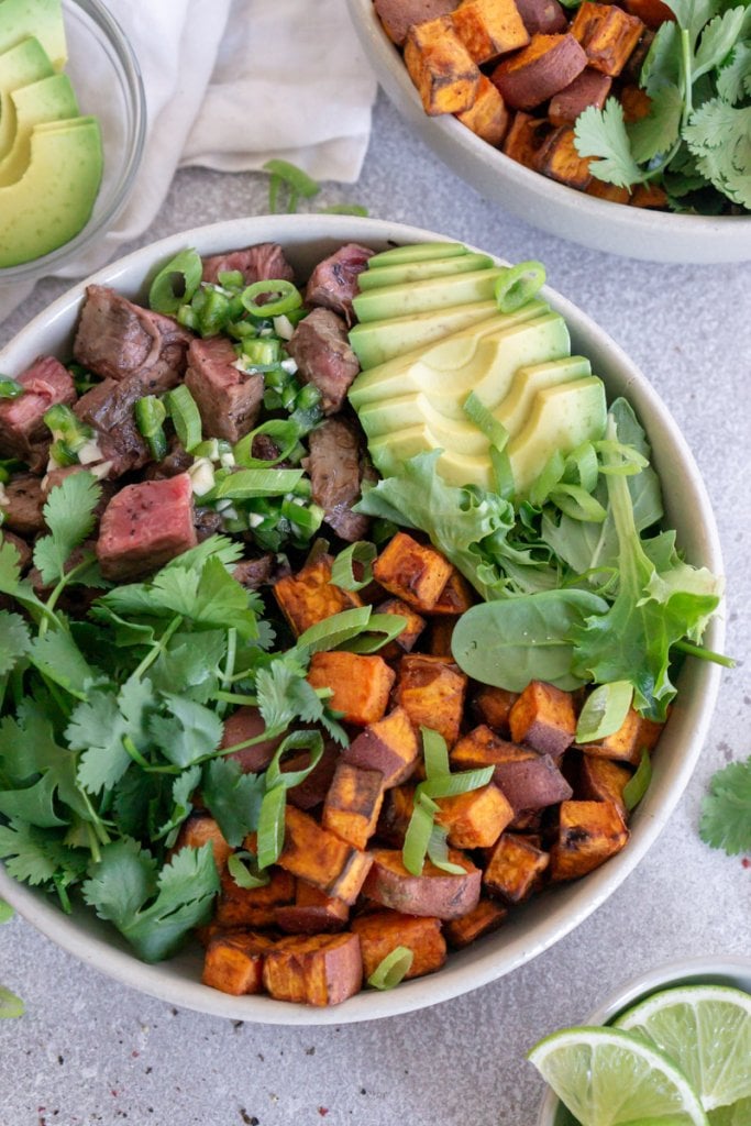 steak bowl with avocado, cilantro, and sweet potatoes with lime wedges on the side