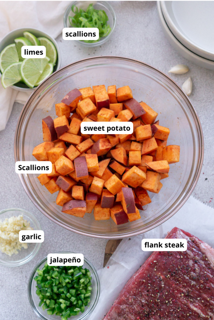cubed sweet potato in a glass bowl with steak, limes, and garlic on the side