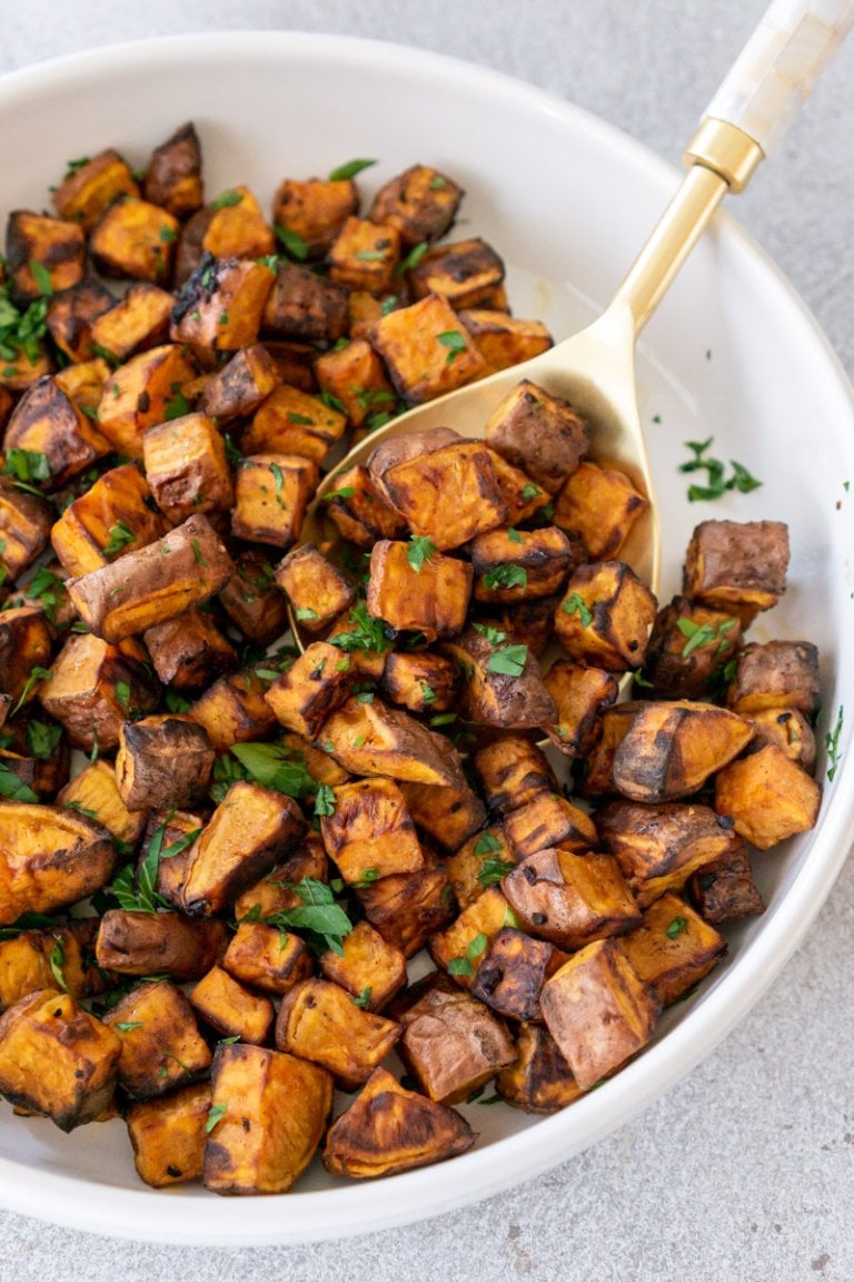 air fryer sweet potato cubes in a white bowl with a serving spoon