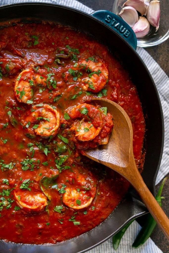 marinara sauce in a cast iron pan with shrimp and a wooden spoon