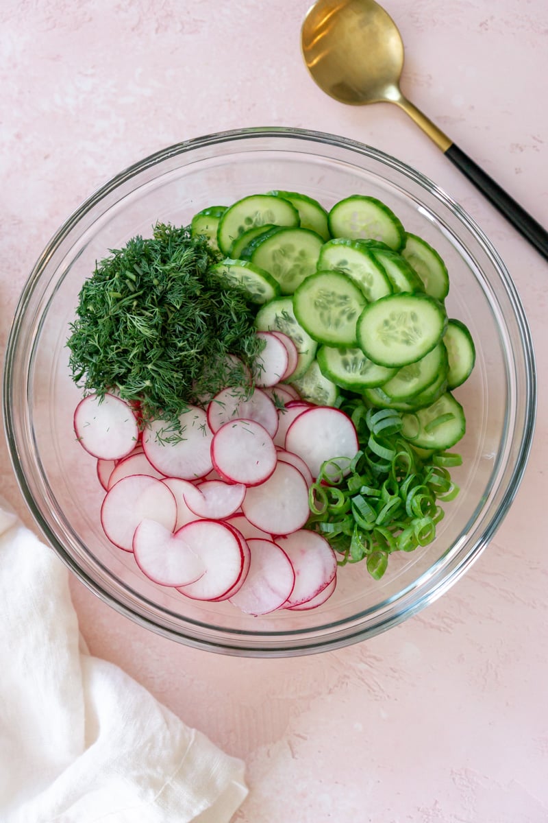 sliced cucumbers, radishes, dill, and green onions, in a mixing bowl.