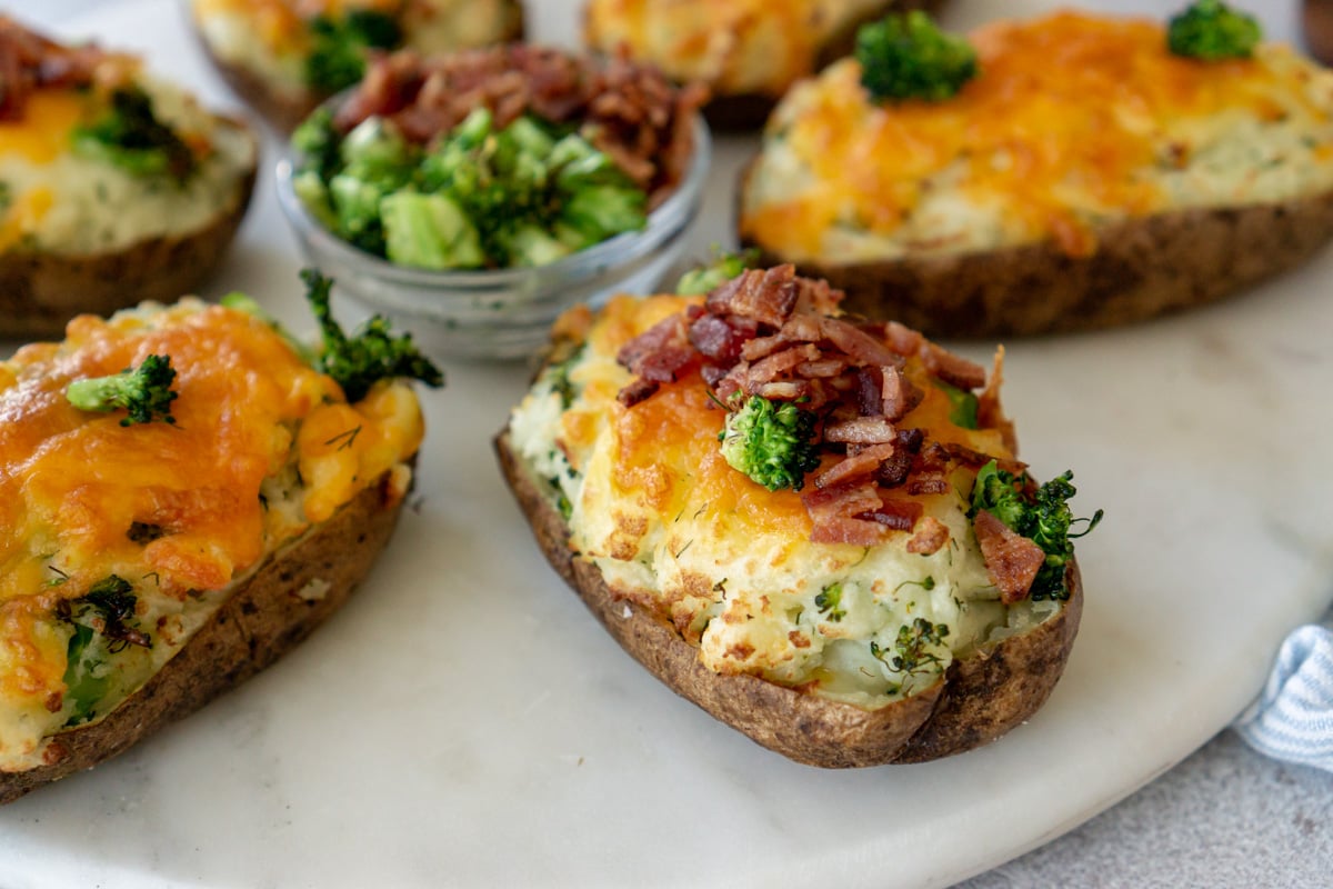 Twice baked potatoes on a serving dish with a bowl of bacon and white onions.