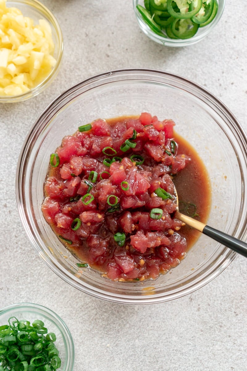 Tuna marinating in poke sauce in a glass bowl with a spoon.