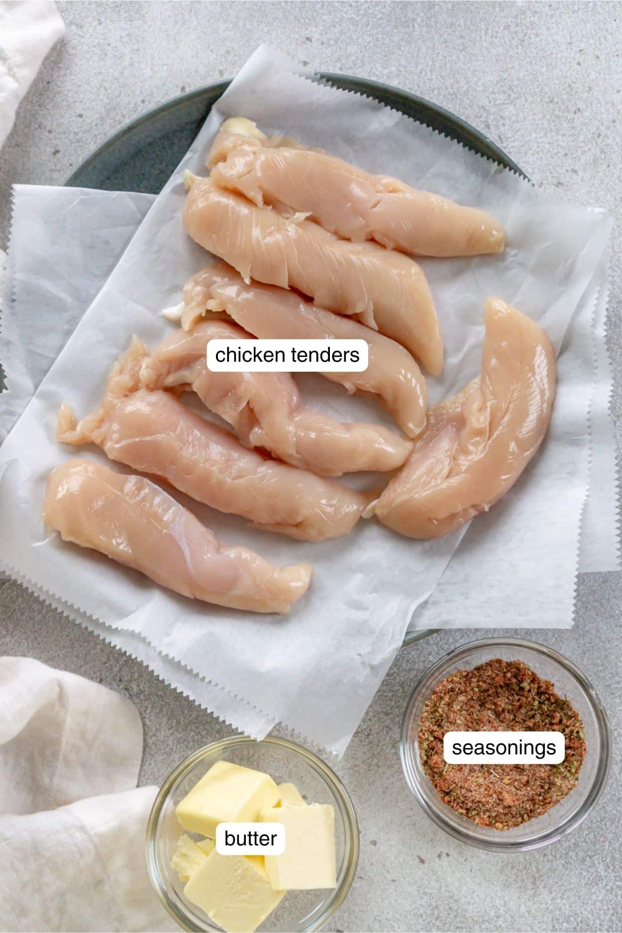 Raw chicken tenders on a plate, next to seasonings and butter in bowls.