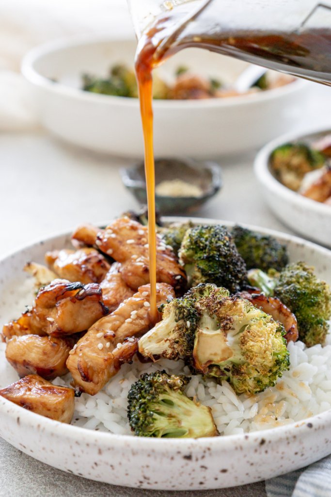 pouring teriyaki sauce on chicken and broccoli with rice