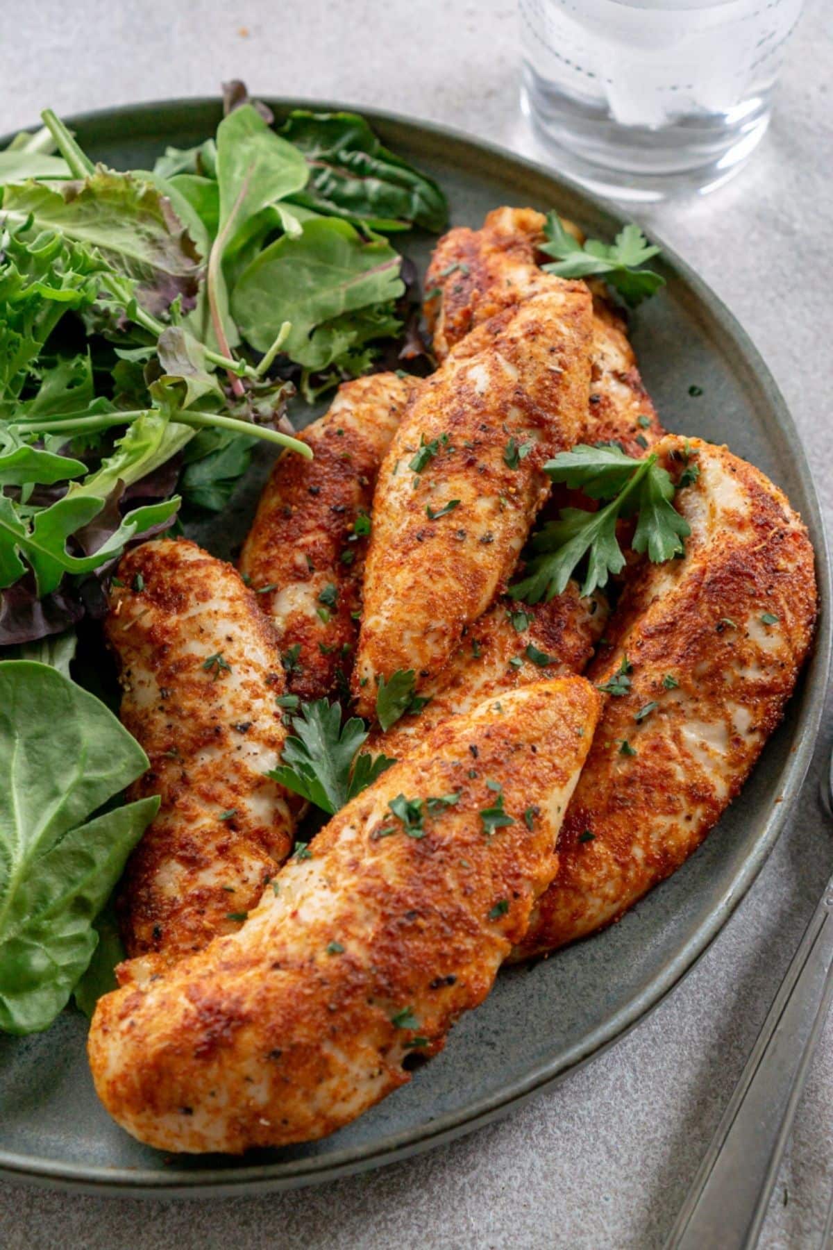 a plate of oven baked chicken tenders with greens on the side.