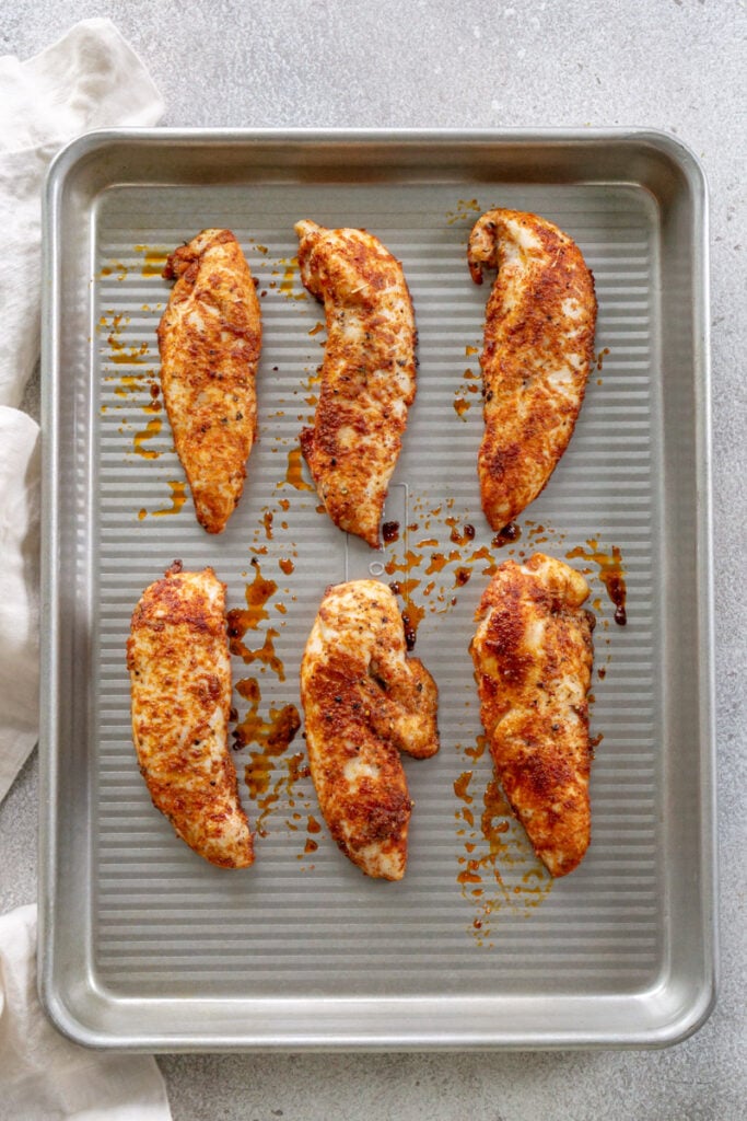 Seasoned, baked chicken tenders on a sheet pan.