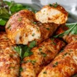 oven baked chicken tenders on a plate and one is sliced in half.