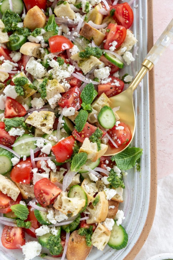 tomato panzanella salad on a serving plate with a gold serving spoon