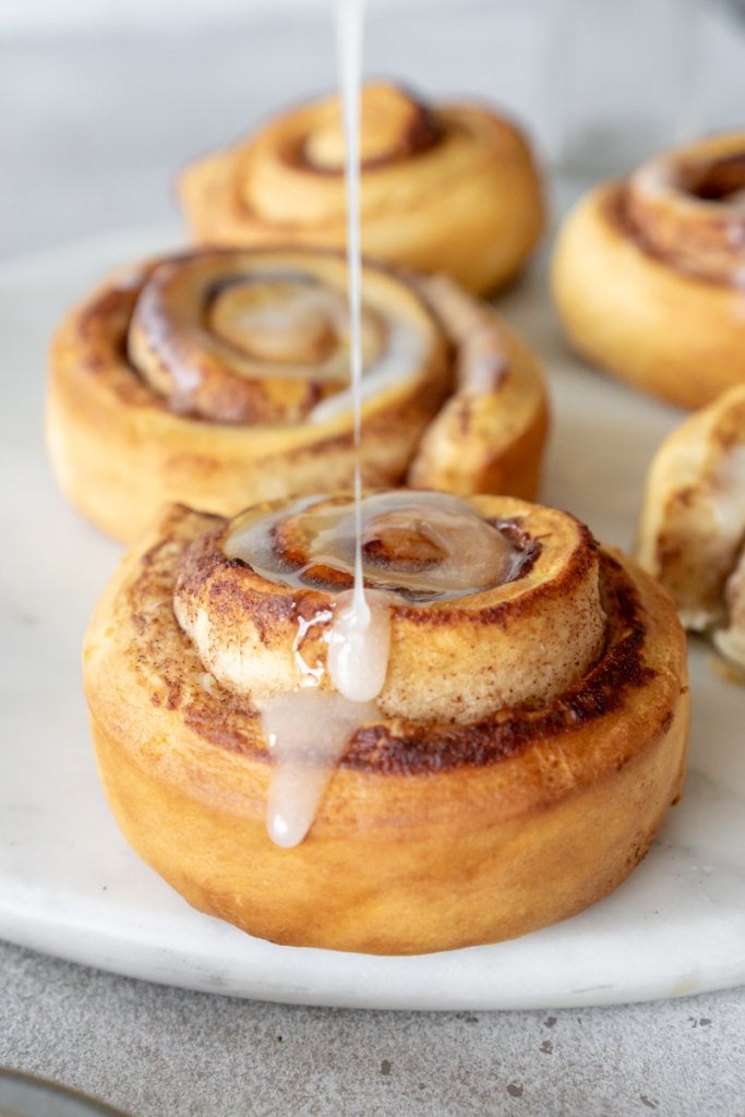 drizzling icing on an air fryer cinnamon roll
