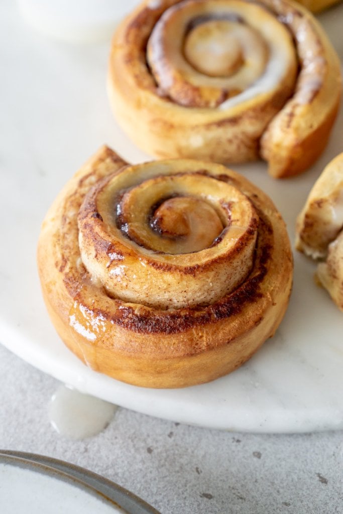 close up of air fryer cinnamon rolls on a marble platter with icing dripping off the side