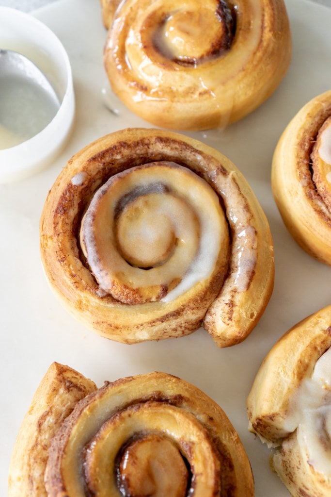 air fryer cinnamon rolls on a marble tray with icing on the side