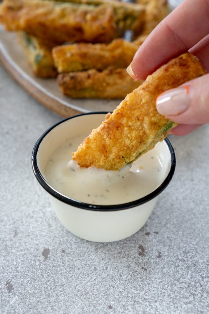 hand dipping a zucchini fry in sauce