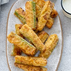 air fryer zucchini fries on a white plate with dipping sauce to the side