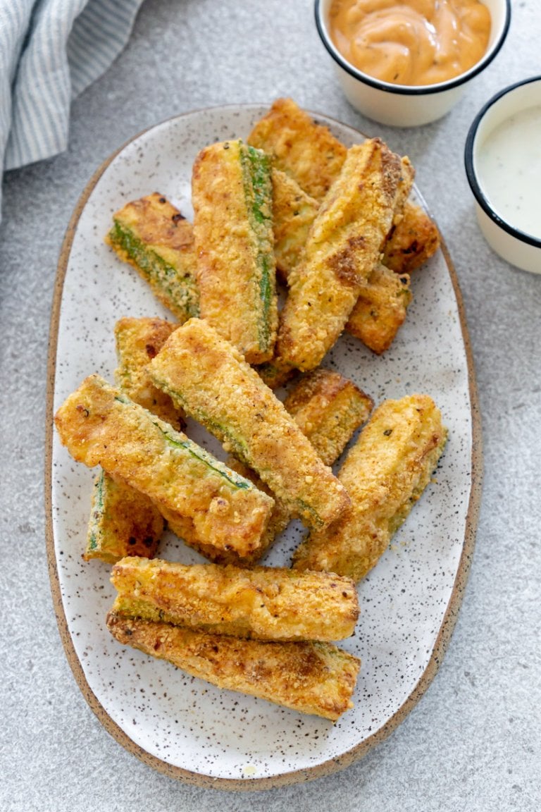 air fryer zucchini fries on a white plate with dipping sauce to the side