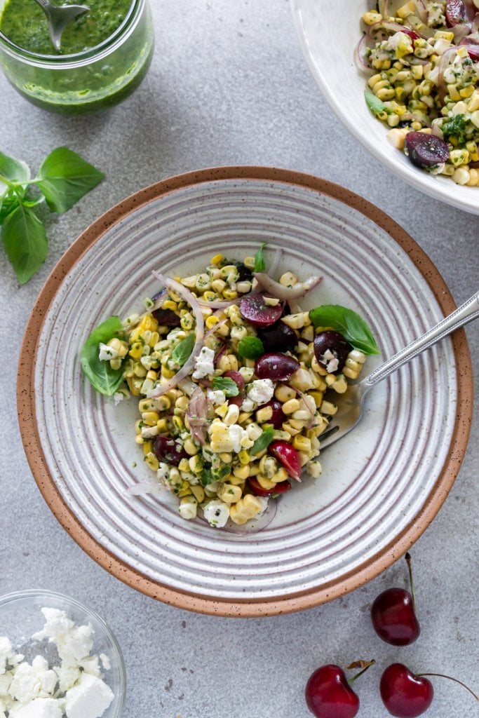 summer corn salad in a bowl with a fork, basil vinaigrette in a jar to the side