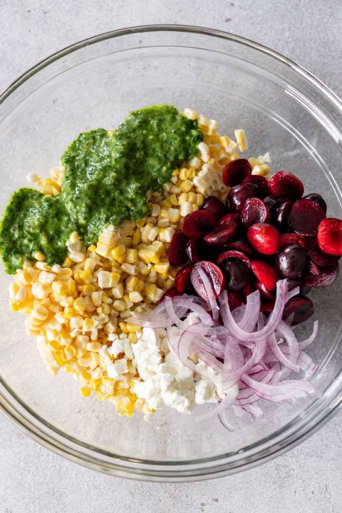 corn, cherries, red onion, cheese, and basil vinaigrette in a bowl