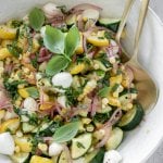 zucchini salad in a large white bowl with gold serving spoons