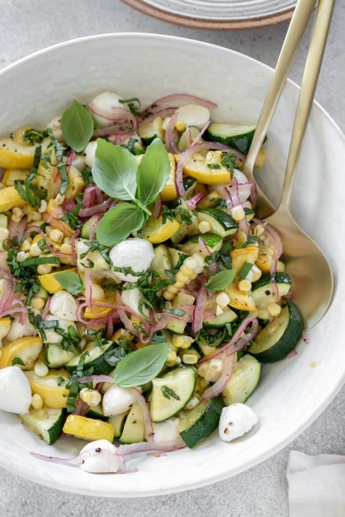 zucchini salad in a large white bowl with gold serving spoons