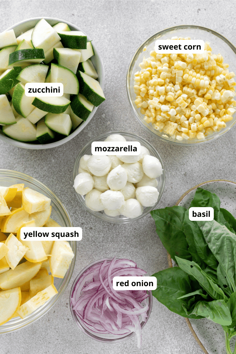 Zucchini, squash, corn, mozzarella, red onion, and basil in small bowls.