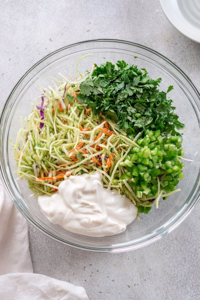 slaw mix, sour cream, mayonnaise, cilantro, and jalapeño in a glass bowl