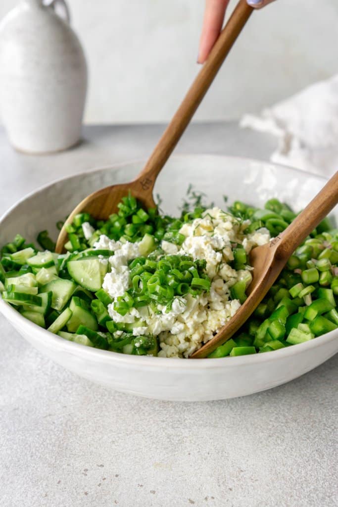tossing vegetables and feta cheese in a serving bowl with wooden tongs