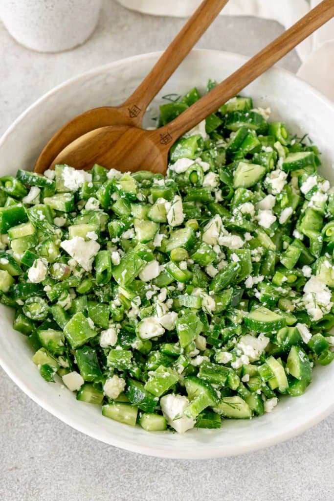 chopped vegetable salad in a white bowl with wooden serving spoons