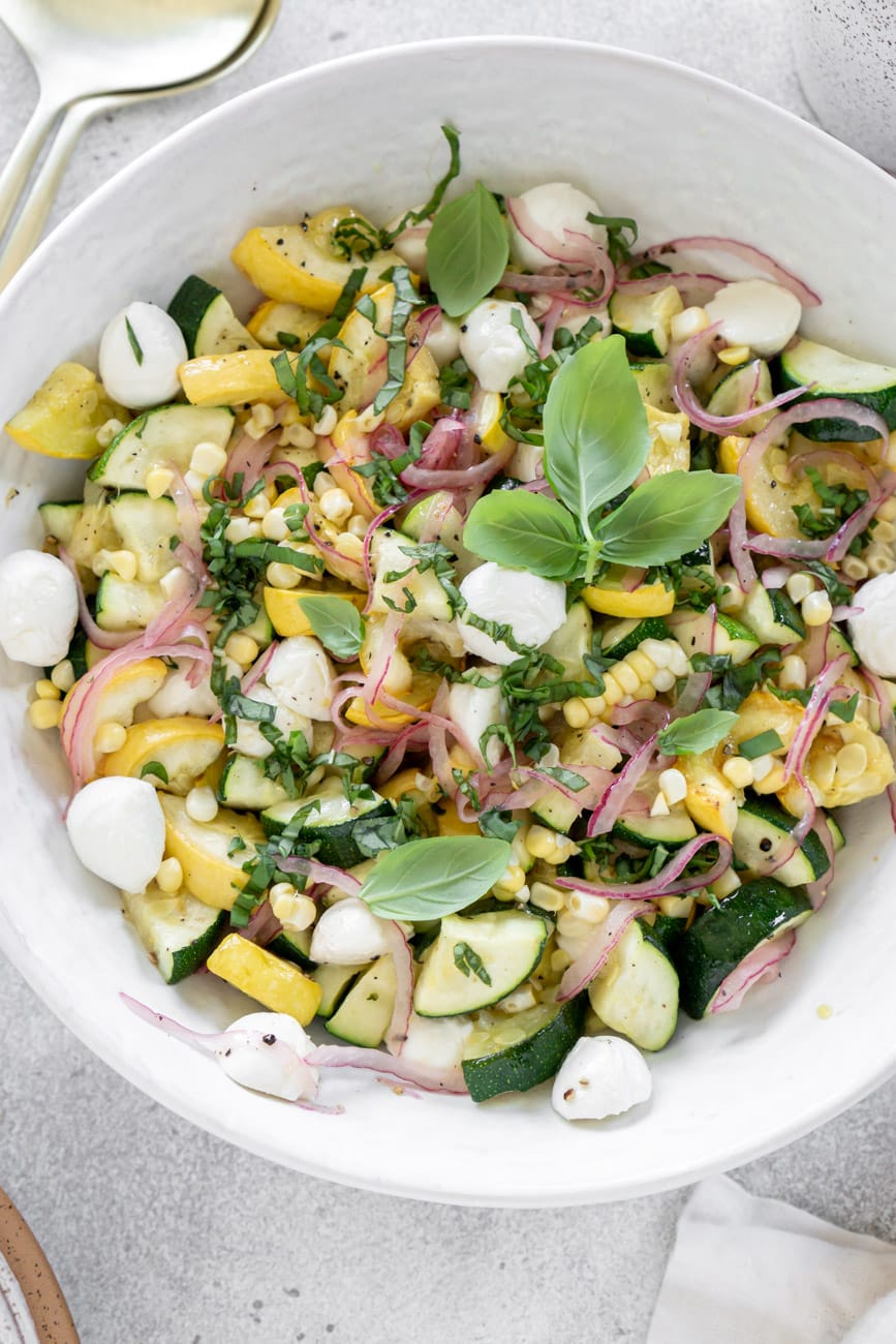 Zucchini salad in a white bowl with basil.