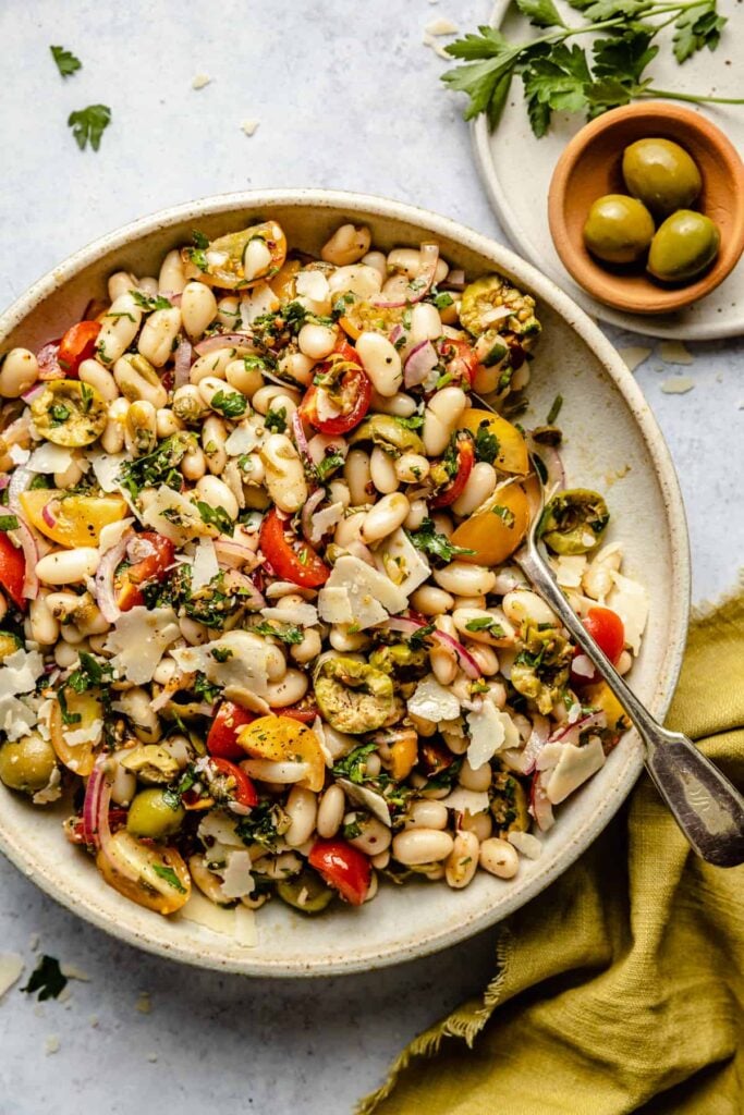 White bean salad in a tan bowl with a spoon inside.