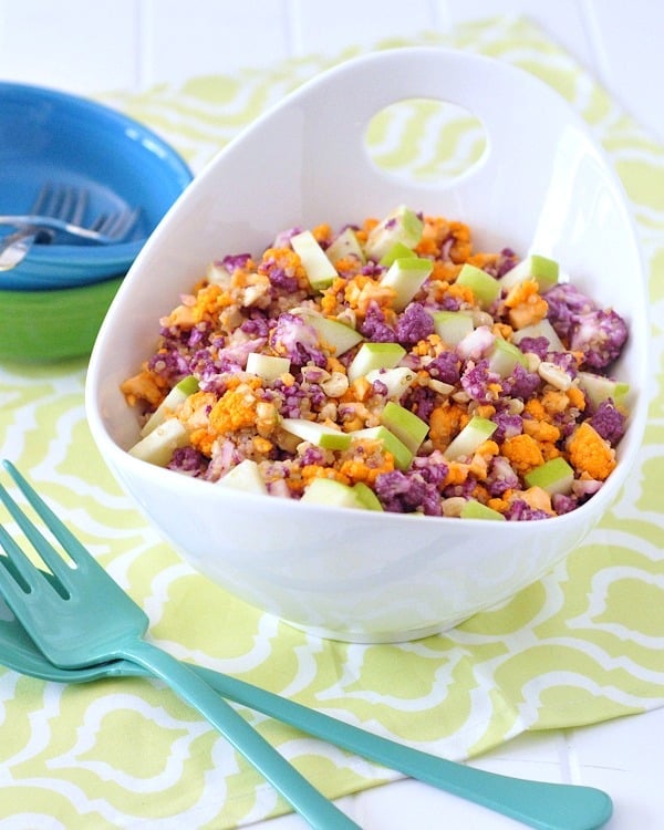 Cauliflower cashew confetti salad in a large white bowl with two forms near the bowl.