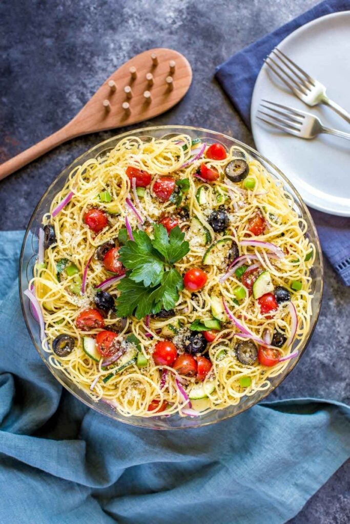 Cold spaghetti salad with herbs, tomatoes, and black olives, in a glass bowl.