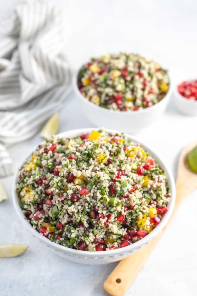 Pomegranate Couscous Salad in a large white bowl with fresh herbs.