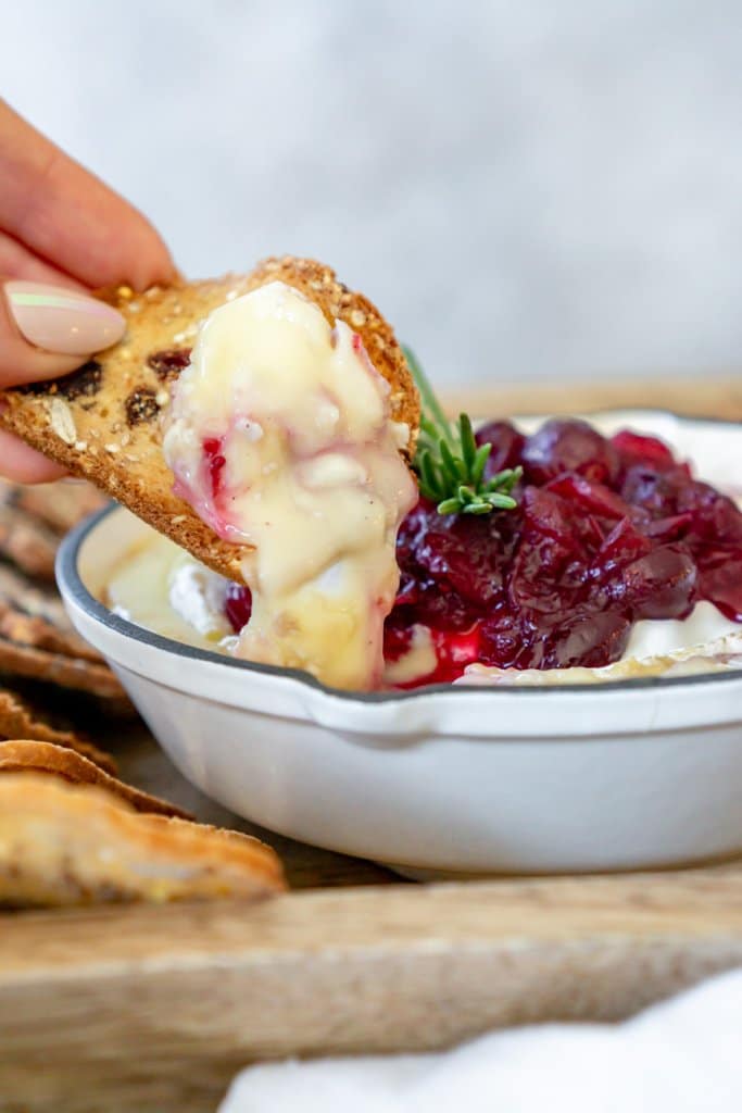 hand dipping a cracker in cranberry baked brie