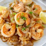 hibachi shrimp with onions on a white plate with lemon wedges