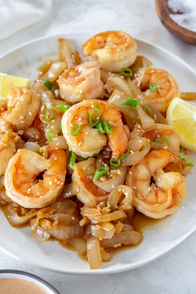 hibachi shrimp with onions on a white plate with lemon wedges