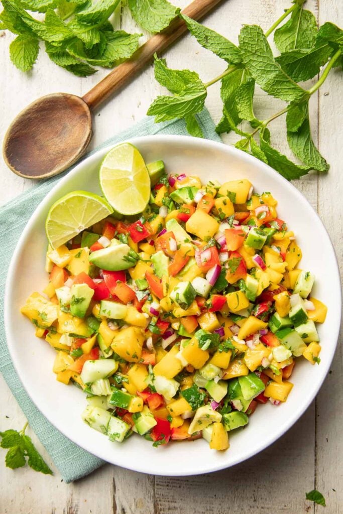 Mango salad with a wooden spoon and fresh greens around it.
