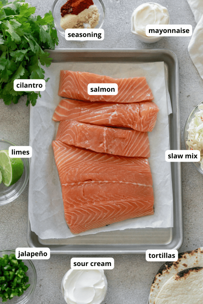 salmon on a sheet pan, cilantro, jalapeno, tortillas, seasoning in a bowl, slaw mix