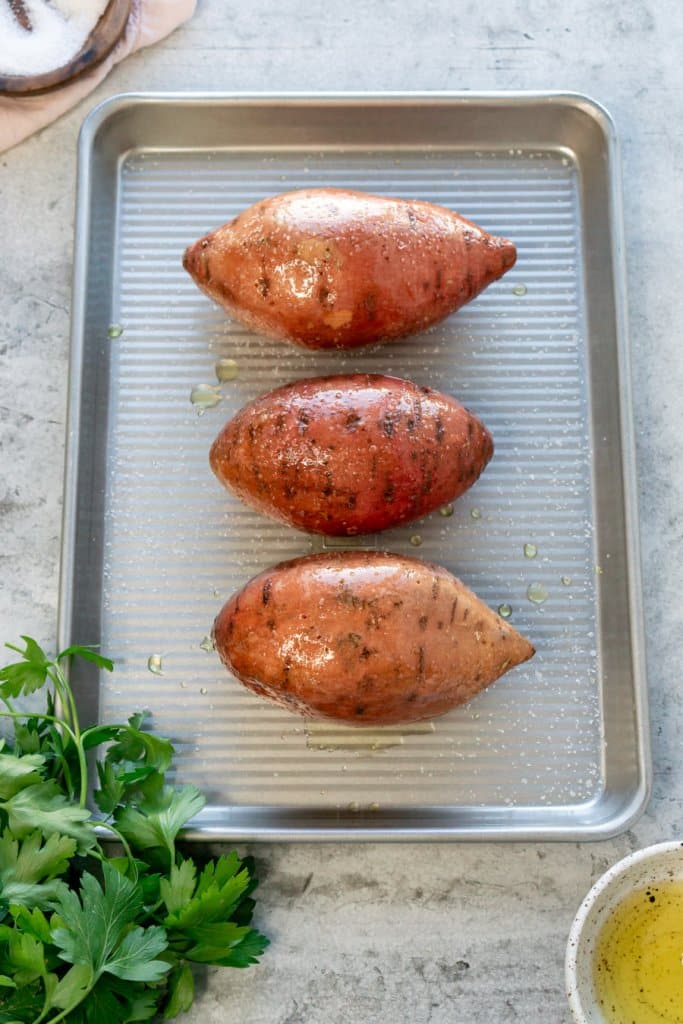 three sweet potatoes on a baking sheet