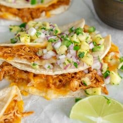 three baked chicken tacos on parchment paper with lime wedges