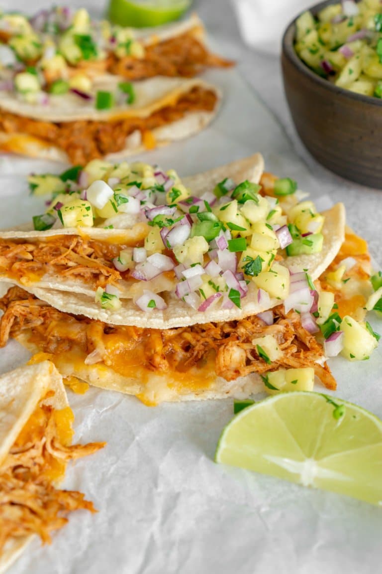 three baked chicken tacos on parchment paper with lime wedges.