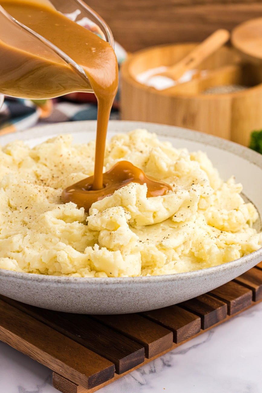 Pouring gravy over mashed potatoes in a bowl.