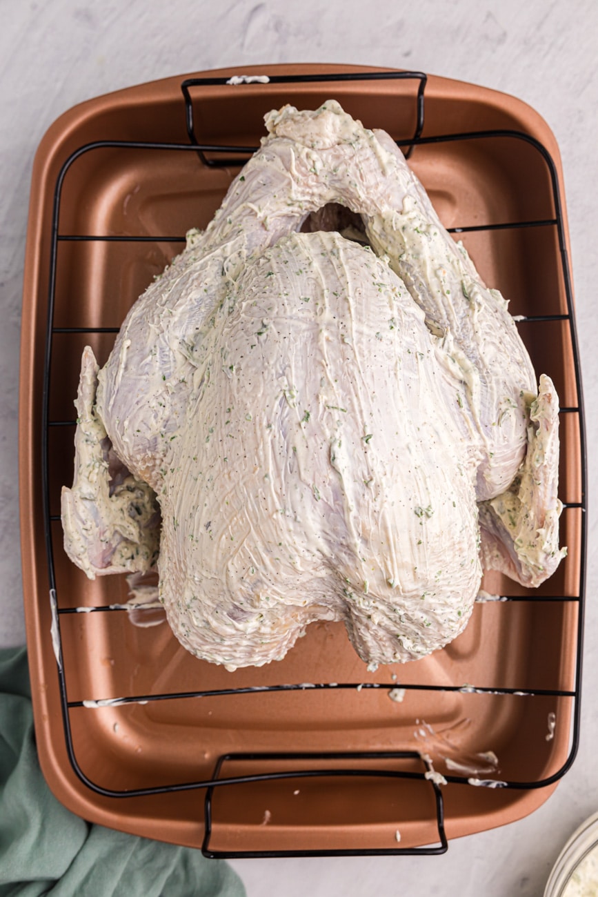 Overhead shot of a turkey in a roasting pan, covered in an herb butter mixture.