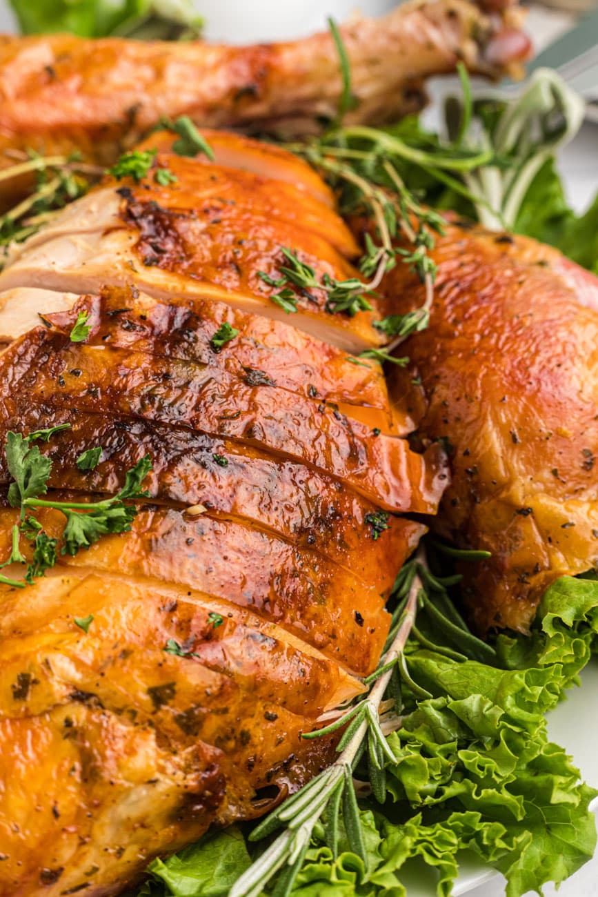 Herb roasted turkey sliced on a platter with lettuce underneath.